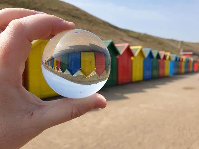 bright coloured beach huts through a lensball