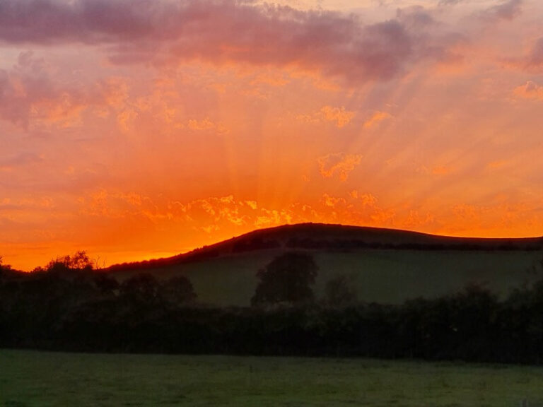 rays of sun at orange sunset over fields