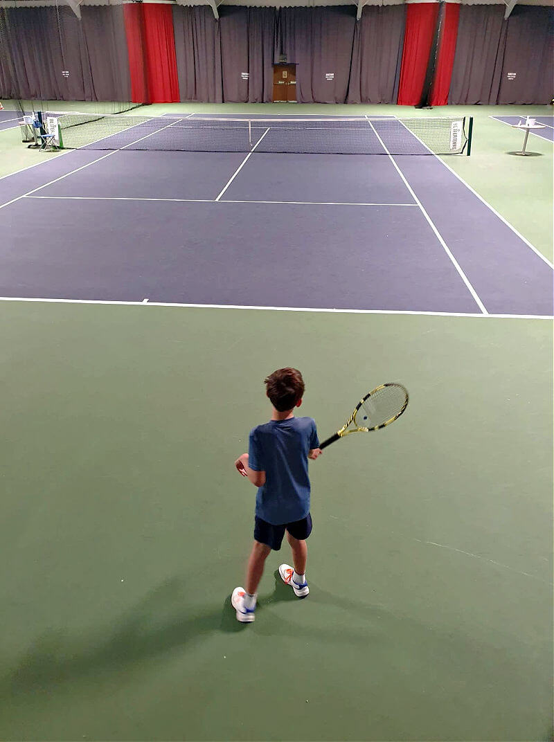 boy standing on edge of indoor tennis court