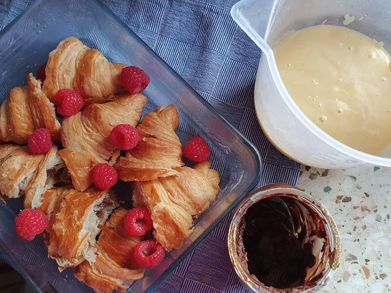 croissants and raspberries with nutella jar and juge of custard