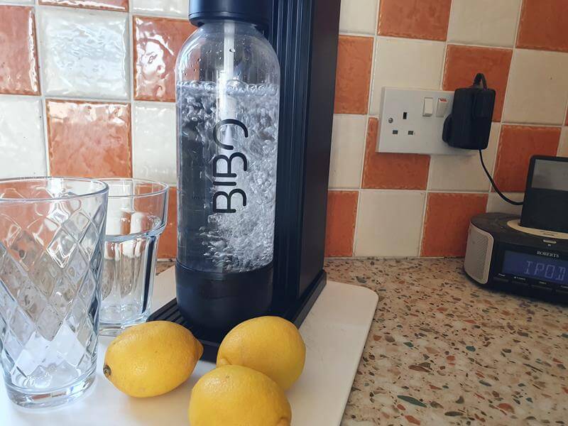 BIBO Fizz with water in and gas making it fizzy with 2 glasses next to it, and 3 lemons