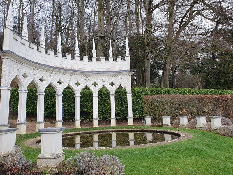 white rococo arched building feature around the side of a pond with reflection