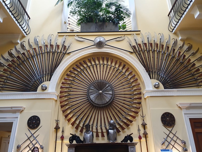 circular display of weapons and others in fan shapes either side in the armoury room