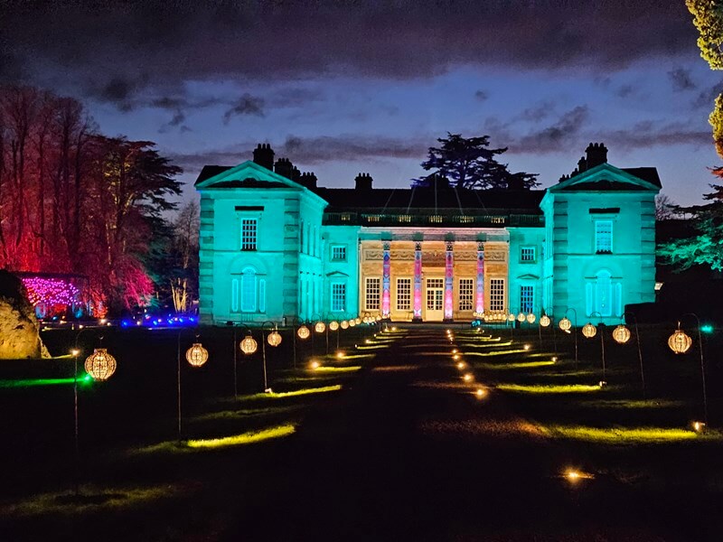 lit up compton verney hall looking down the driveway with lit lanterns along the walkway