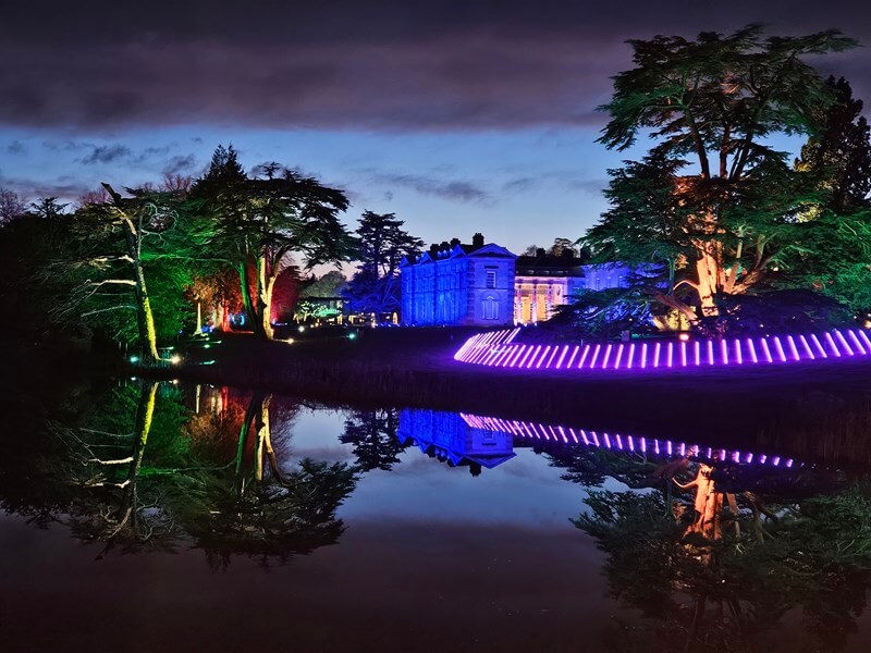 view over lake at Compton Verney looking at the hall and lit up trees and lights all reflected