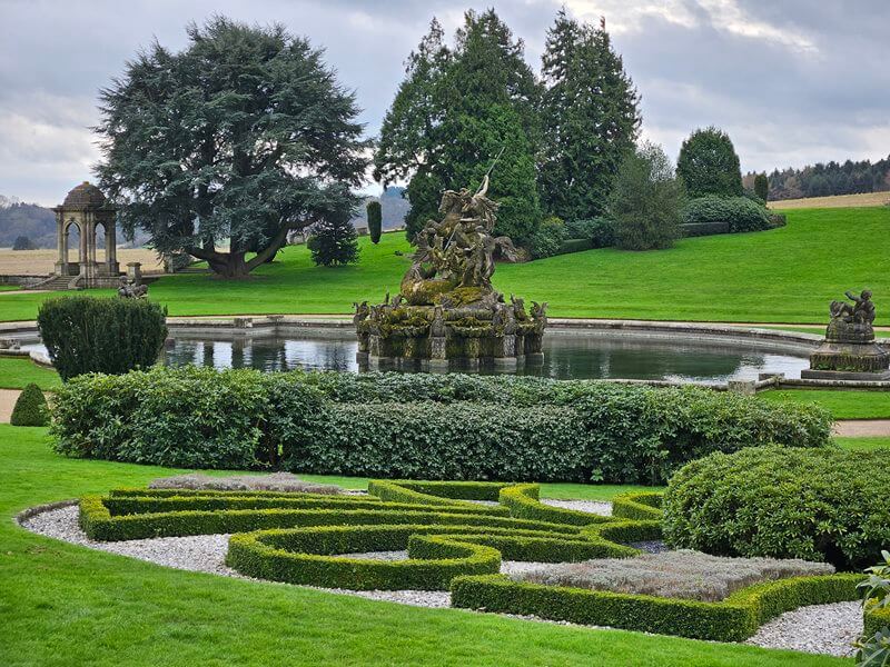 topiary cut hedge pattern in front of pond with water fountain