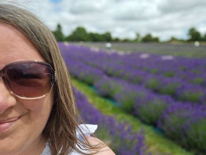 half selfie of woman wearing sunglasses with lavender field rows behind