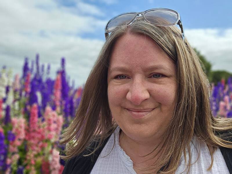 selfie of woman with sunglassed on head in front of delphiniums