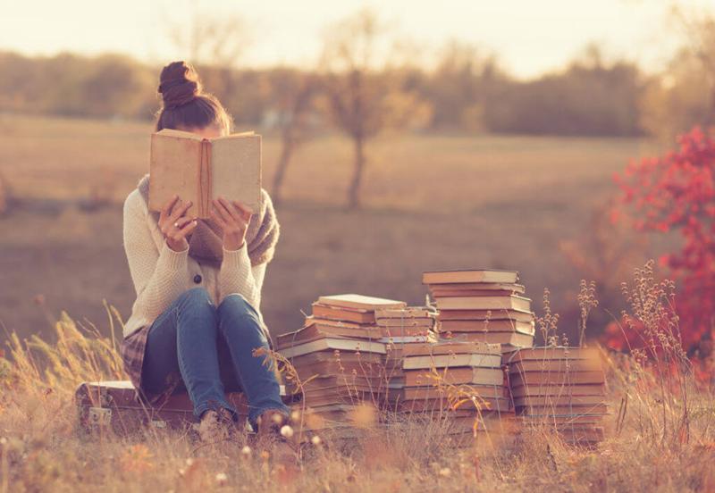 girl reading book in a field with lots of books beside her