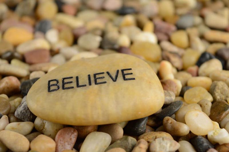 believe text on a large stone on a pebble beach