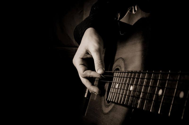 close up man playing guitar focused on guitar and hand strumming in monochrome