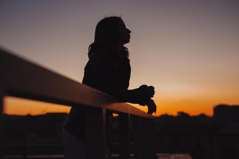 girl silhouette leaning on fence against sunset