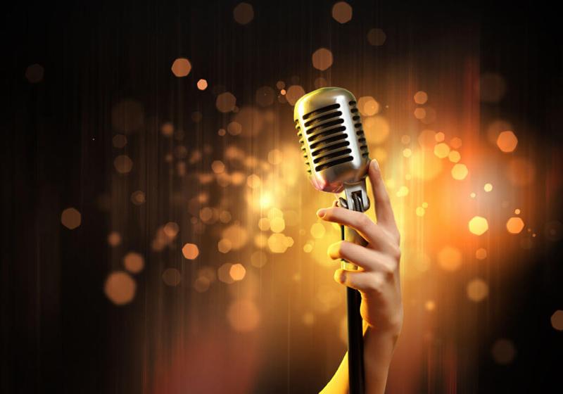 girls hand holding a silver microphone on stand with yellow sparkly lights against a black background