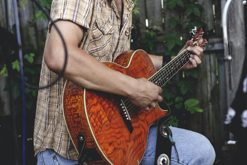 man in checked shirt playing acoustic guitar close up on guitar and body