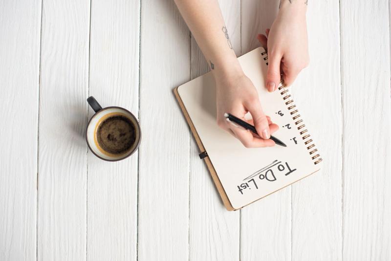 woman writing a to list with a coffee upside down to camera